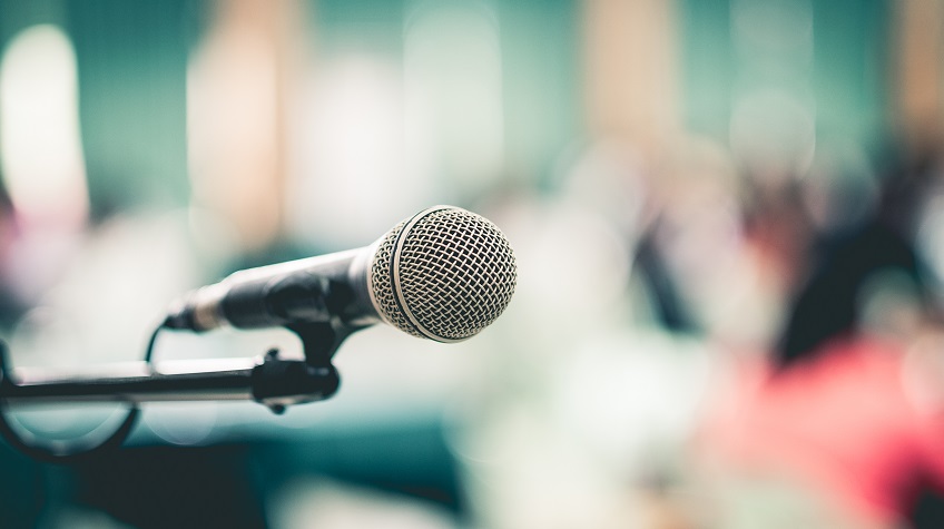 Microphone in focus in the foreground with a blurred meeting in the background.