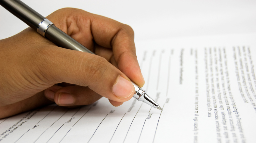 Close up of a hand holding a pen filling out a paper form.