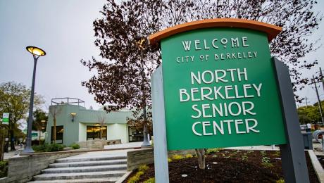 Photo of a green sign saying North Berkeley Senior Center with the senior center building in the background.