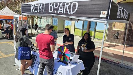 Berkeley Rent Board table at a community event. Two people approach table with two people behind the table.